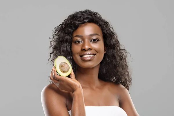 Portrait of attractive black woman with avocado half over gray background — Stock Photo, Image