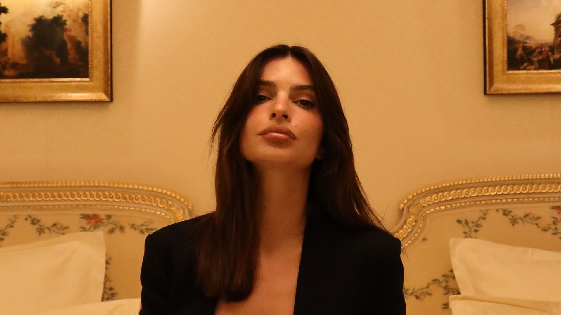 Emily Ratajkowski rocks plunging pantsuit on bed in luxury Paris hotel as she takes on fashion week in City of Lights