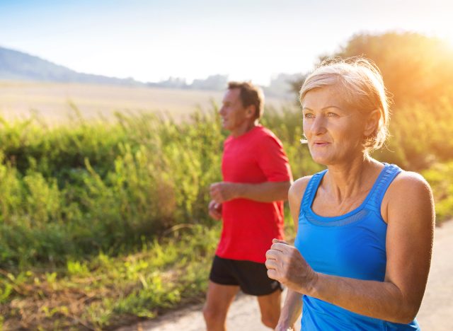 active senior couple walking outdoors in the summertime on trail, demonstrating benefits of exercise one hour a week