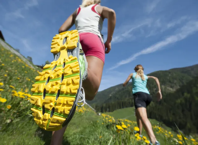 close-up bottom of running shoe, two women running through field, concept of worst running shoes hurting your feet