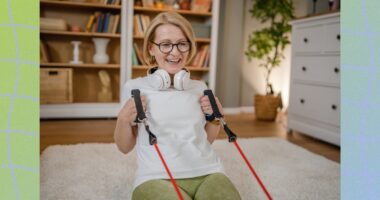 happy older woman with glasses doing resistance band floor exercise in living room