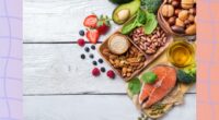 healthy fats like avocado, salmon, olive oil, and nuts on white wood table