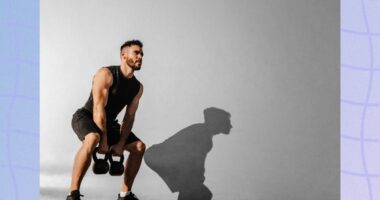 muscular man lifting two kettlebells outdoors in front of cement wall