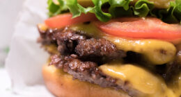 A closeup of the double cheeseburger with tomato lettuce and onion, from Shake Shack.