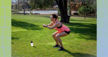 middle-aged woman in pink tank top and black shorts doing squats in park on sunny day