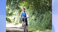 middle-aged woman riding bike outdoors on sunny day surrounded by foliage