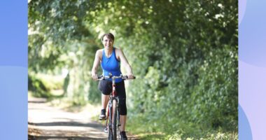 middle-aged woman riding bike outdoors on sunny day surrounded by foliage