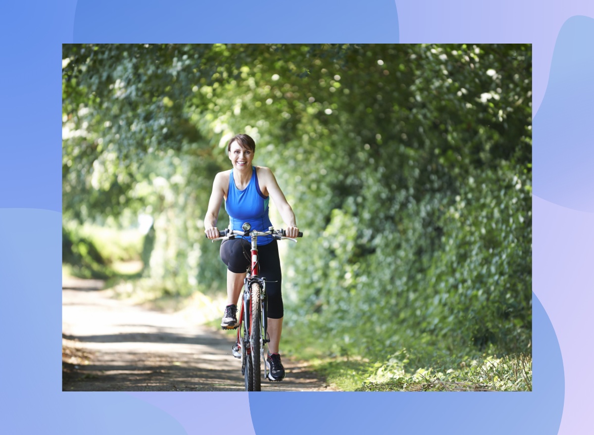 middle-aged woman riding bike outdoors on sunny day surrounded by foliage