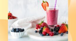 fresh fruit smoothie in tall glass surrounded by fresh berries on white countertop