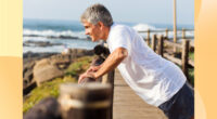 fit senior man doing incline pushups on a beach walk railing