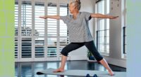 mature woman doing lunge yoga exercise at home in bright living space next to windows