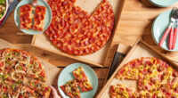 three donatos pizza pies on a wooden table with plates and hands taking slices of pizza