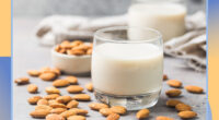 glass of almond milk with almonds laying around it