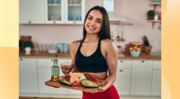 happy fitness woman holding tray of healthy, protein-packed foods in bright kitchen