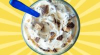 A closeup of a frozen custard concrete, mixed with candy bar pieces and set against a vibrant yellow background.