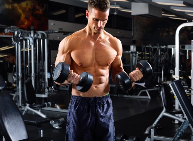 muscular man doing dumbbell bicep curls, concept of regular strength exercises for men