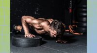 fit, muscular man doing weight plate pushups in dark gym