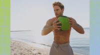 fit, shirtless man doing medicine ball workout on the beach