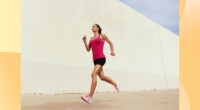 fit woman in pink tank top and black shorts running outdoors on pavement on sunny day