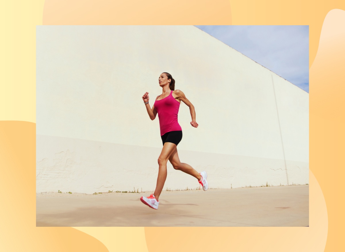 fit woman in pink tank top and black shorts running outdoors on pavement on sunny day