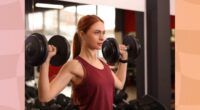 fit, determined red-haired woman doing dumbbell shoulder presses at the gym in the weight room