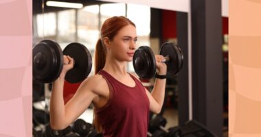 fit, determined red-haired woman doing dumbbell shoulder presses at the gym in the weight room