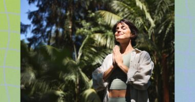 fit brunette woman meditating outdoors in the sunlight among lush green vegetation