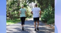 mature couple walking for exercise on path surrounded by trees on sunny day