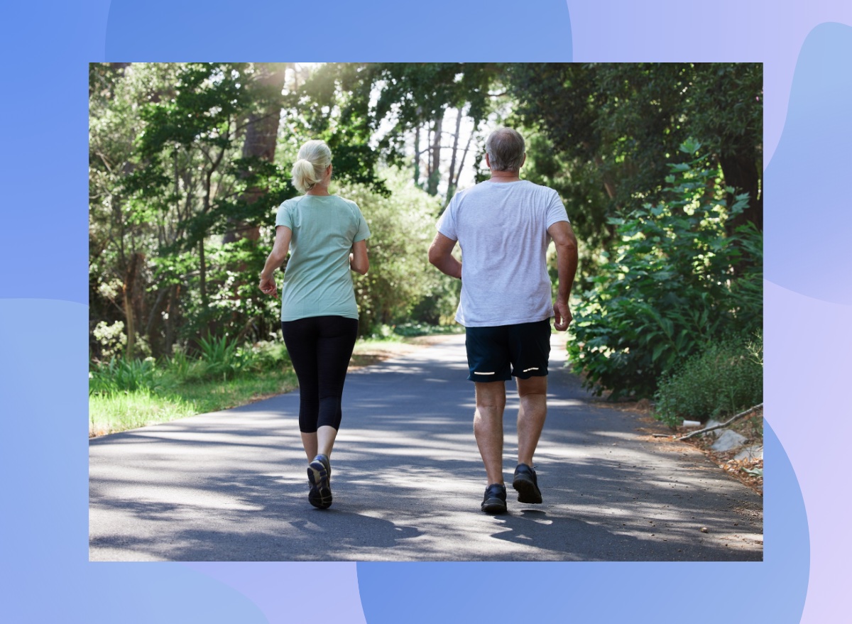 mature couple walking for exercise on path surrounded by trees on sunny day