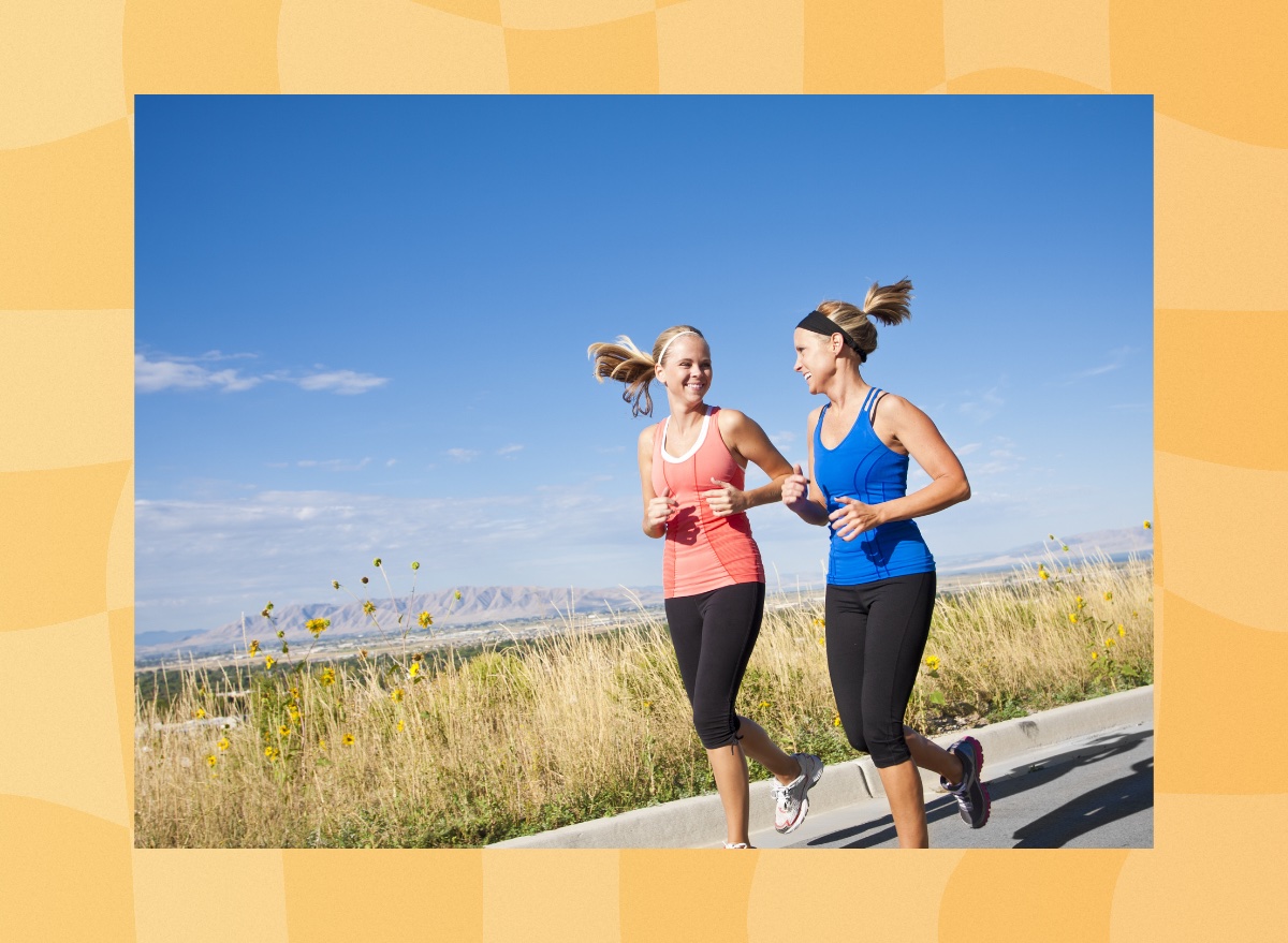 two fit female friends running outdoors on a scenic trail on sunny day