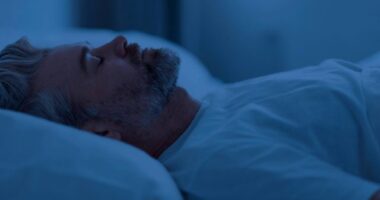 mature man sleeping on his back in bed in dark room at night