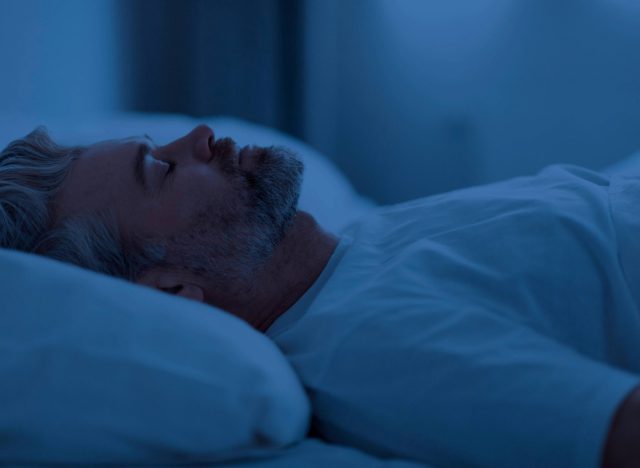 mature man sleeping on his back in bed in dark room at night