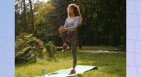 focused woman doing single-leg balance exercise on yoga mat in field on sunny day