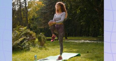 focused woman doing single-leg balance exercise on yoga mat in field on sunny day