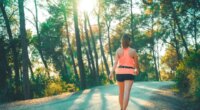 woman doing walking workout uphill on street with sunlight coming through trees