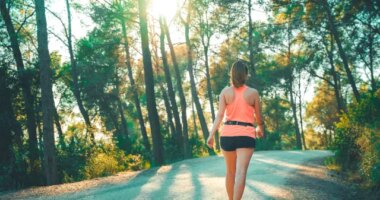 woman doing walking workout uphill on street with sunlight coming through trees