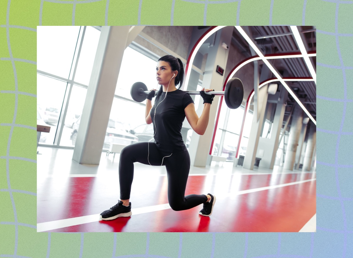 focused brunette woman doing barbell lunge on an indoor track at the gym