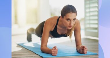 focused woman doing forearm plank on bright blue yoga mat in sunny room