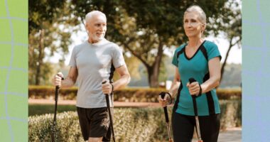 mature couple taking a brisk walk with walking poles along path in park on a sunny day