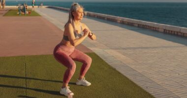 mature woman doing squats on turf by the water