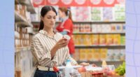 focused brunette woman reading food label at the grocery store with full shopping cart