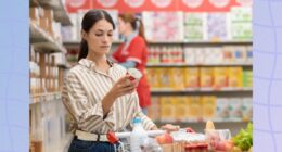 focused brunette woman reading food label at the grocery store with full shopping cart