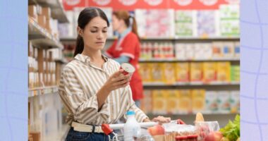 focused brunette woman reading food label at the grocery store with full shopping cart