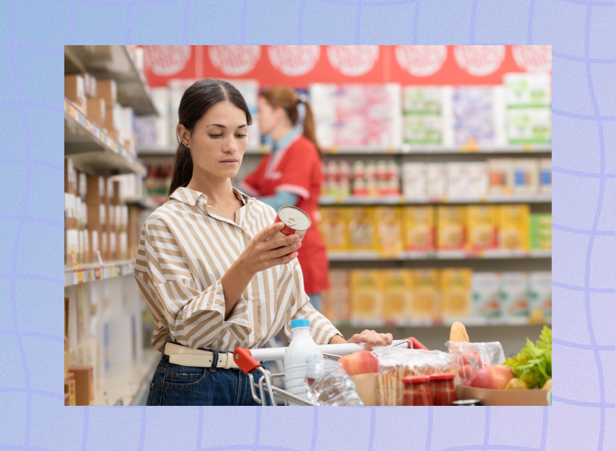 focused brunette woman reading food label at the grocery store with full shopping cart