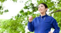 happy woman in blue jacket walking for exercise outdoors under green foliage