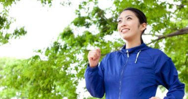 happy woman in blue jacket walking for exercise outdoors under green foliage