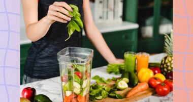 close-up of woman making fresh juice in blender with vegetables