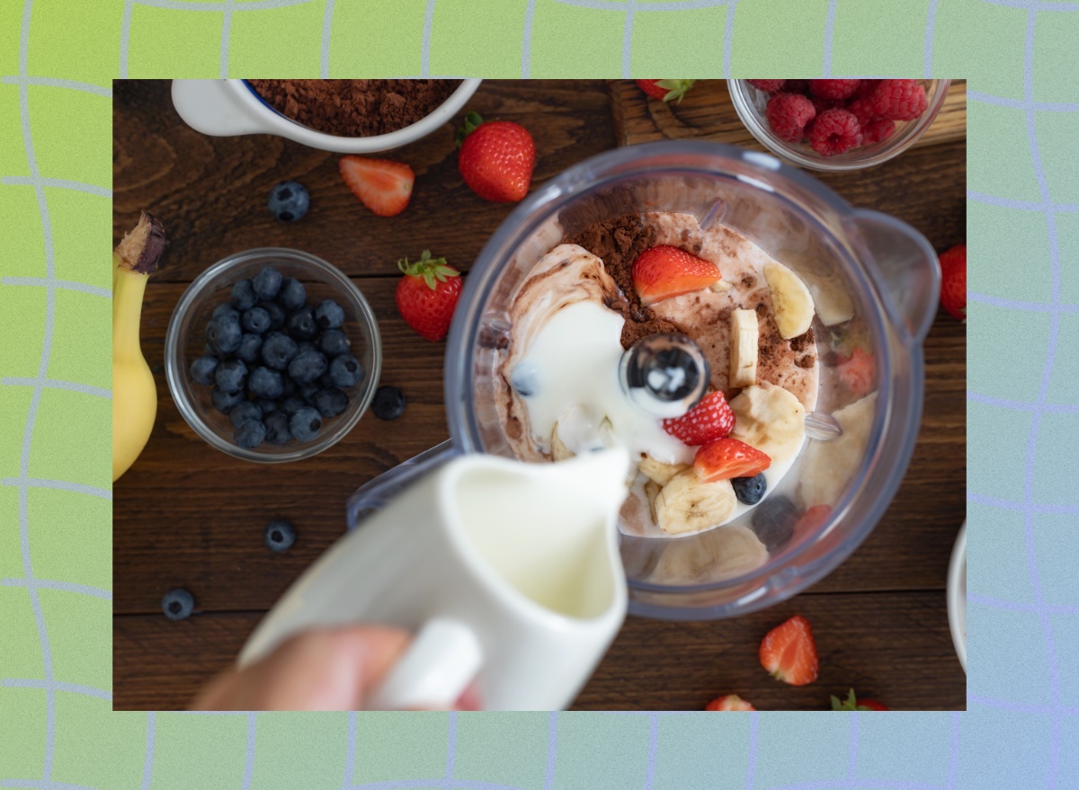 close-up of hand making fresh fruit protein shake with milk, chocolate protein powder, and berries