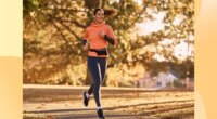 happy brunette woman running for exercise on park trail on sunny autumn day