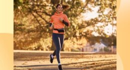 happy brunette woman running for exercise on park trail on sunny autumn day